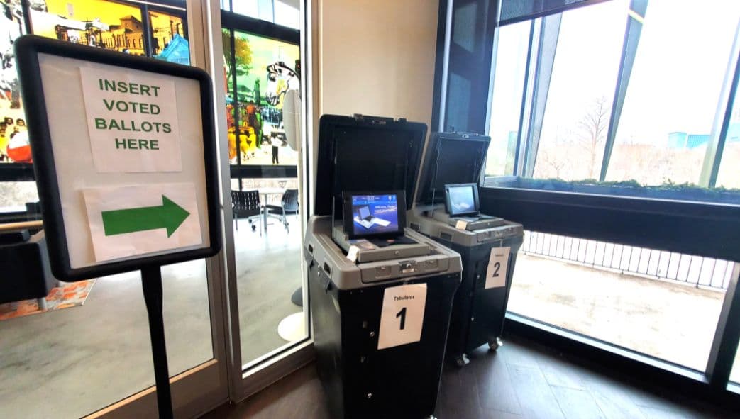 A ballot tabulator beside a sign directing voters where to insert ballots.